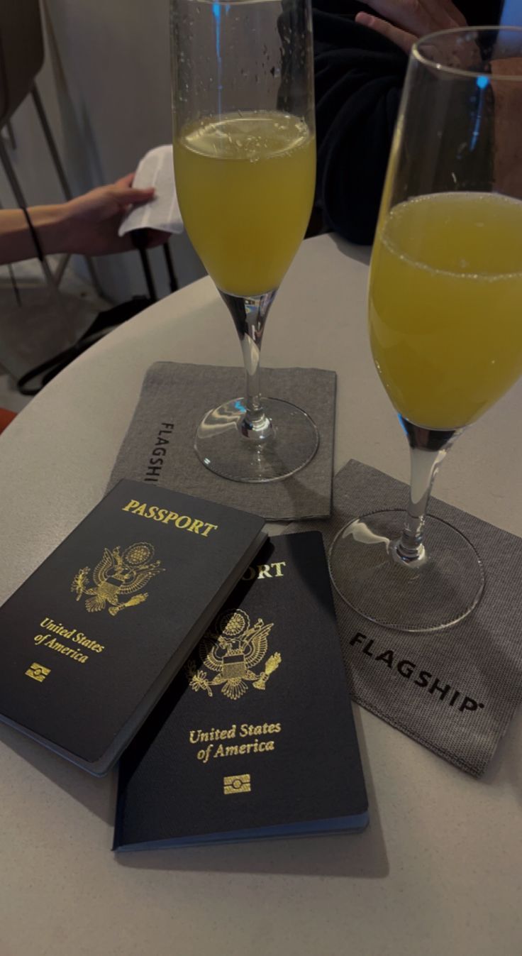 three passport coasters sitting on top of a table next to two glasses of wine