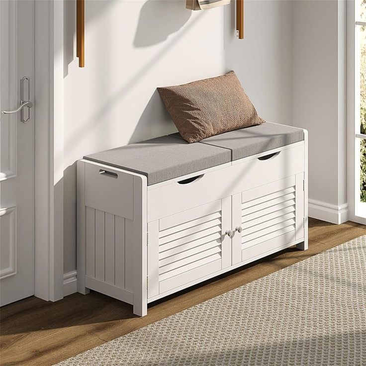 a white storage bench with two drawers and a cushion on top, in front of a window