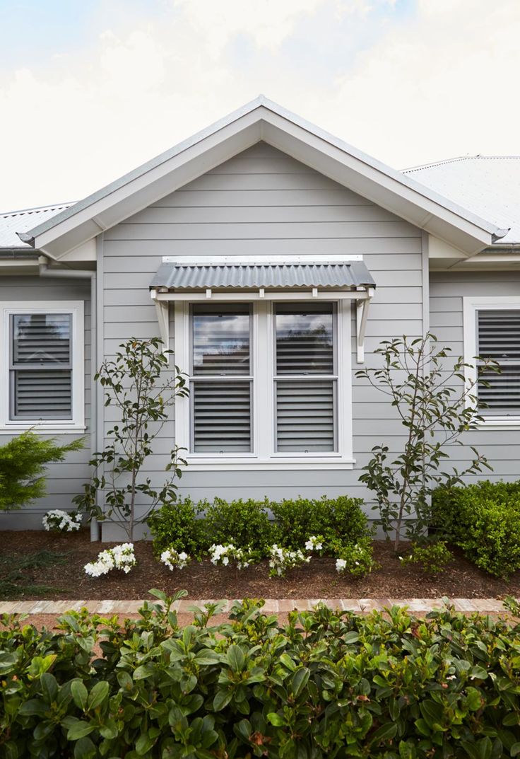 a gray house with white shutters and bushes