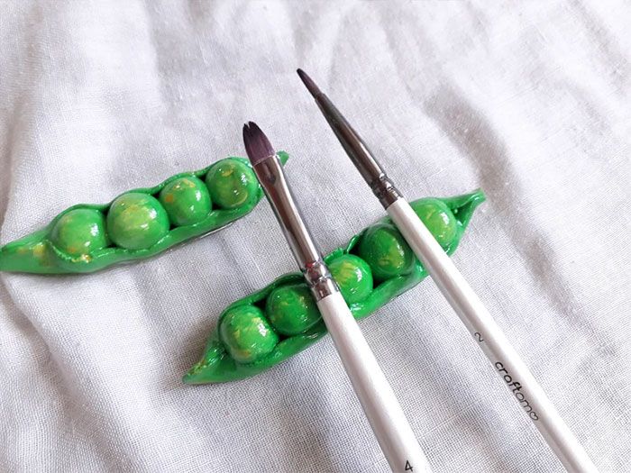 two green peas sitting next to each other on top of a white cloth with paintbrushes