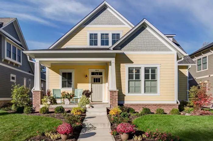 a yellow house with white trim on the front door and windows, along with landscaping