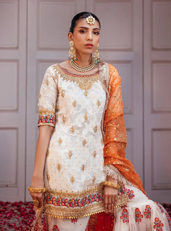 Embrace the essence of tradition and elegance with our stunning Chunri chiffon off-white ensemble, adorned with intricate machine work and heavy hand embroidery on the neck, hem, and sleeves. Paired perfectly with an organza embroidered gharara, accentuated with light handwork and scattered chan, creating a harmonious blend of texture and elegance. The look is completed with a gradient organza dye block print dupatta, embellished with sequin and gota spray and the finishing of jamwar and kiran a Semi-stitched Sharara With Embroidered Border For Reception, Unstitched Off White Sharara With Embroidered Border, Fitted Salwar Kameez With Embroidered Border For Reception, Elegant White Anarkali Set With Embroidered Border, Festive Off-white Embroidered Sharara, Traditional Off White Sharara With Embroidered Border, Bollywood Style Dress With Embroidered Border For Reception, Elegant Traditional Wear With Embroidered Border In Off White, Festive Off White Sharara With Embroidered Border