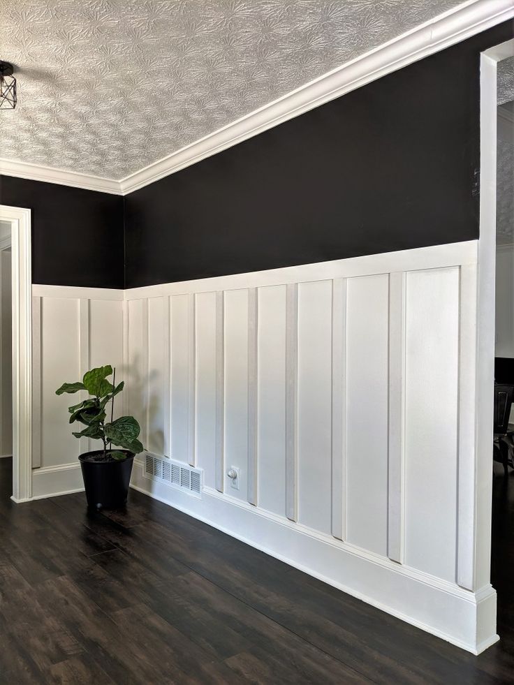 an empty room with black and white walls, wood floors and a potted plant