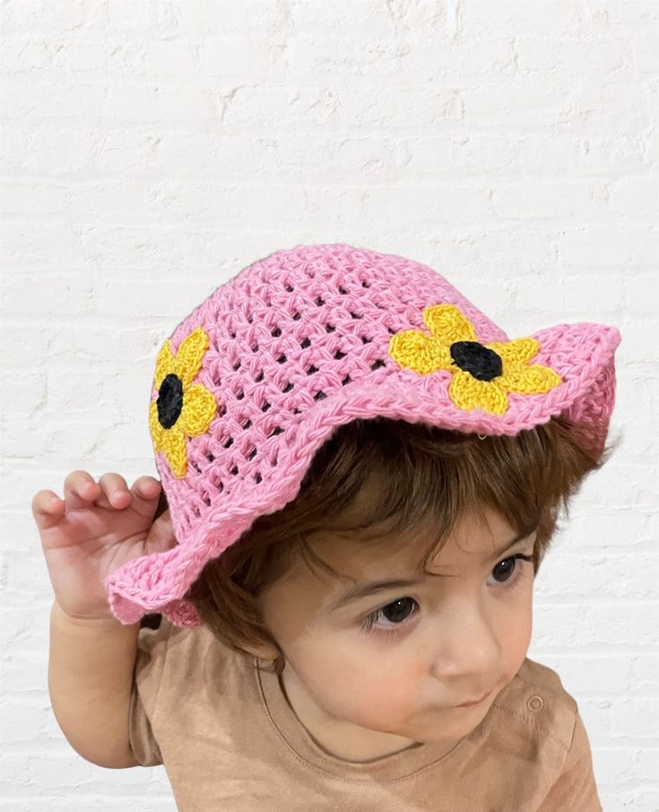 a small child wearing a pink crocheted hat with yellow flowers on it's brim