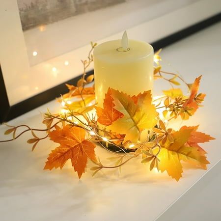 a lit candle surrounded by autumn leaves on a table with a framed photograph in the background