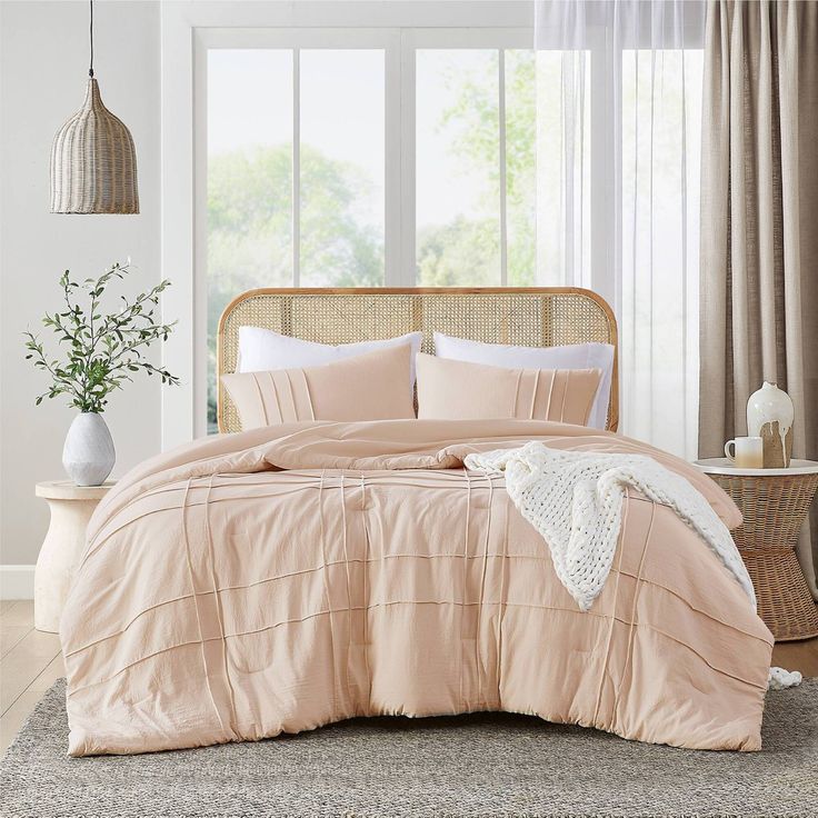 a bed in a bedroom with pink comforter and pillows on top of it, next to a window