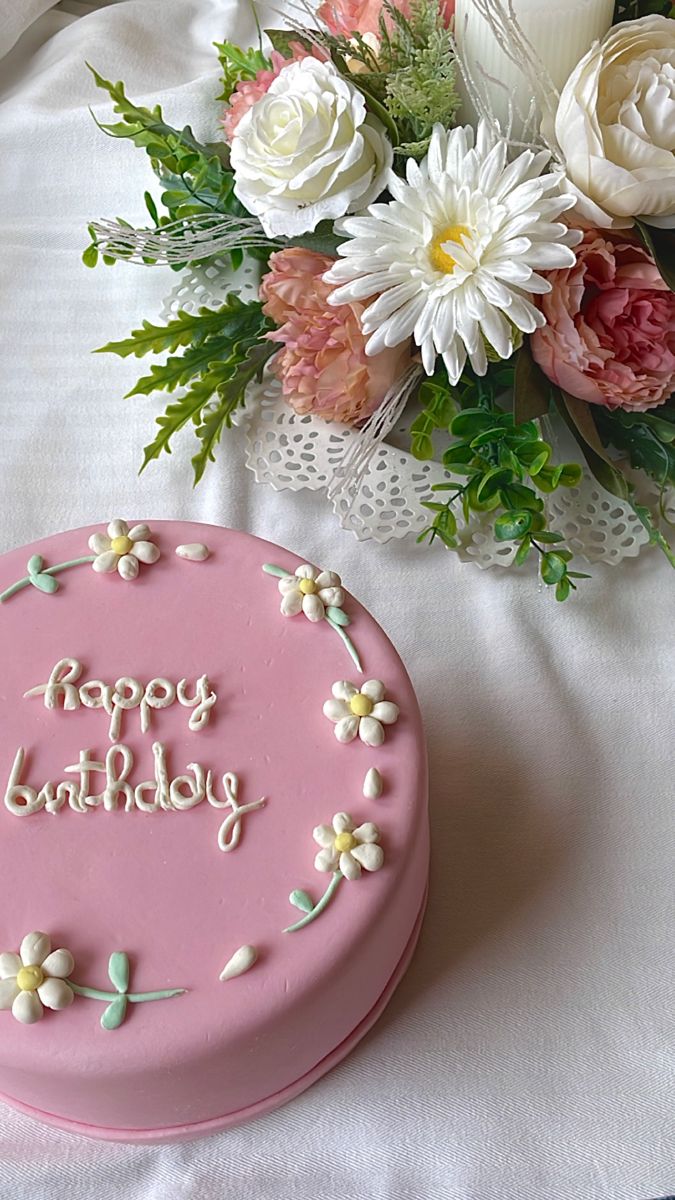 a pink birthday cake sitting on top of a table next to a bouquet of flowers