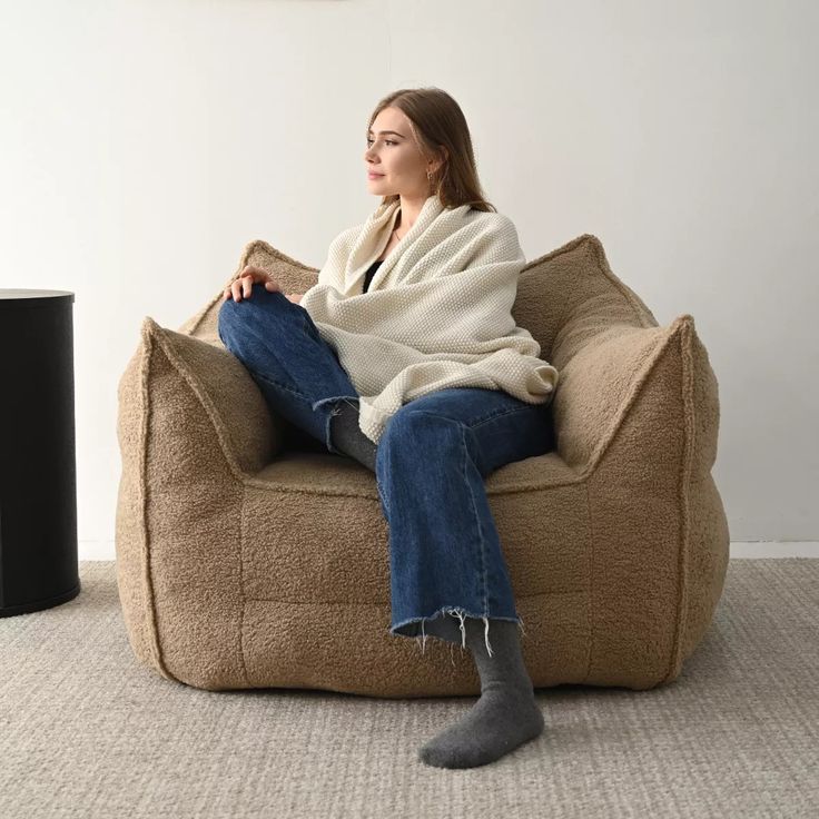 a woman sitting on a bean bag chair with a blanket draped over her head and legs