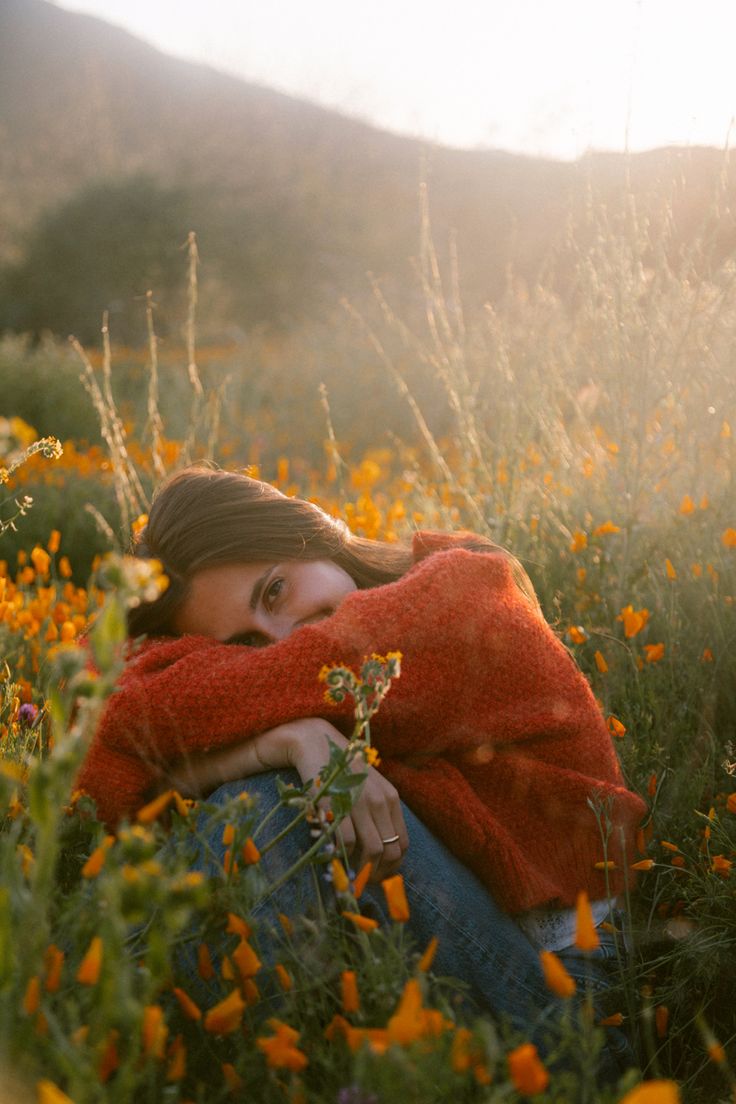 a woman is sitting in the grass with her arms around her neck