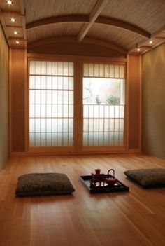 an empty room with wooden flooring and windows in the corner, including two teapots on trays