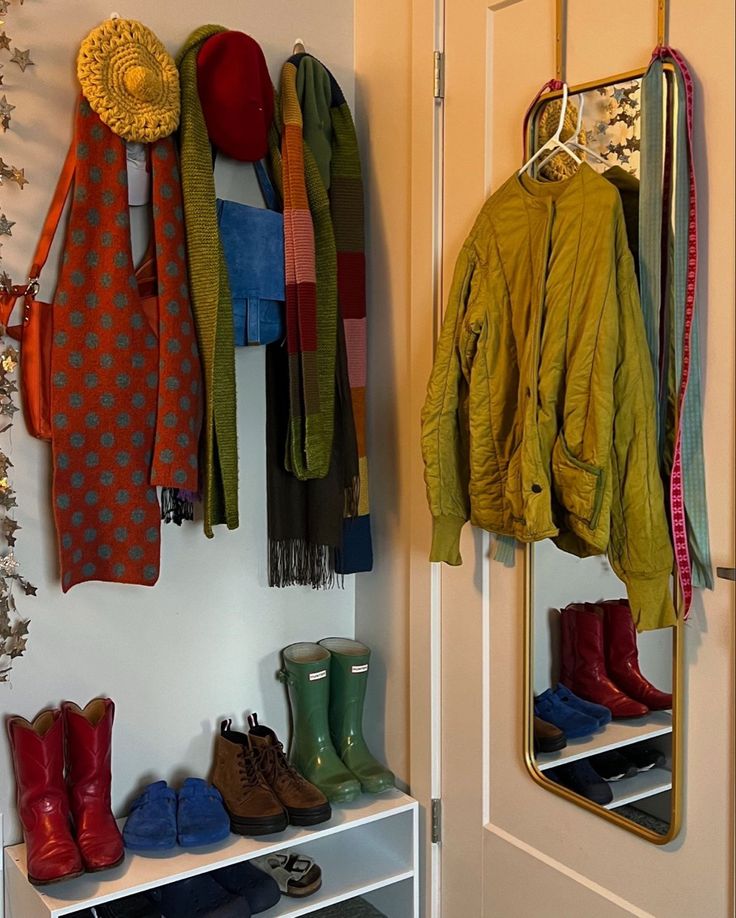 a coat rack filled with boots and scarves next to a white wall mounted mirror