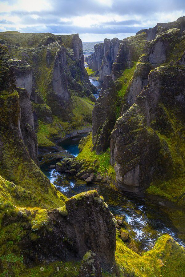 a river flowing through a lush green valley next to tall rocks and grass covered hillsides