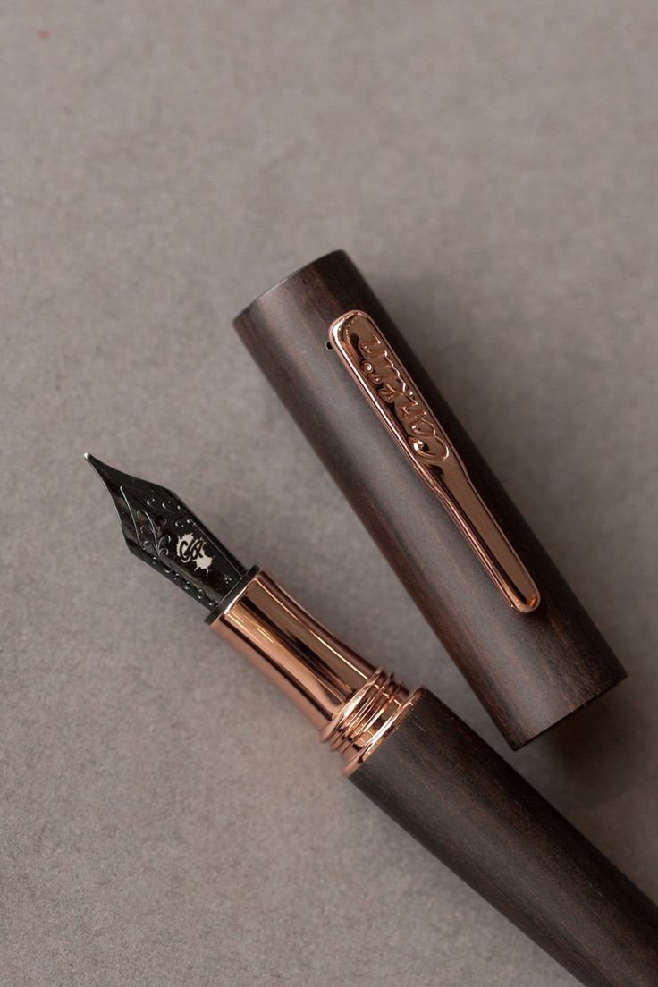 two fountain pens sitting next to each other on top of a gray surface with gold trim