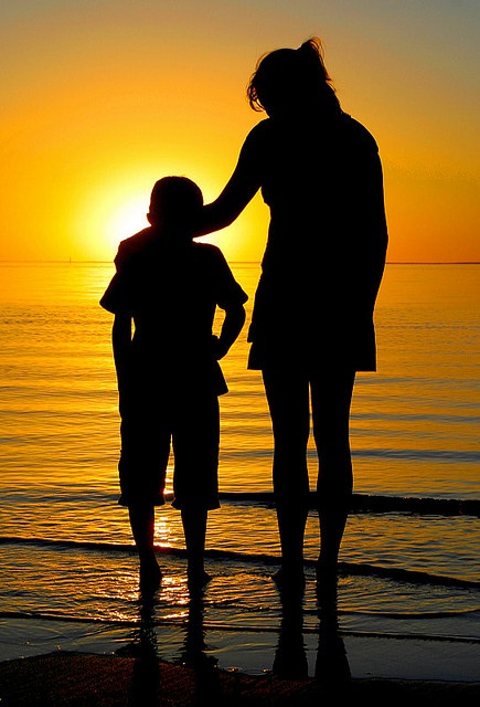 a mother and son are silhouetted against the sunset at the beach while holding hands