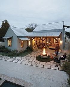 a person sitting in front of a house with a fire pit on the patio and an open porch