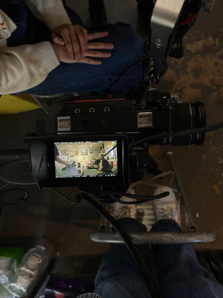 a person sitting down with a camera on their lap and another person standing in the background