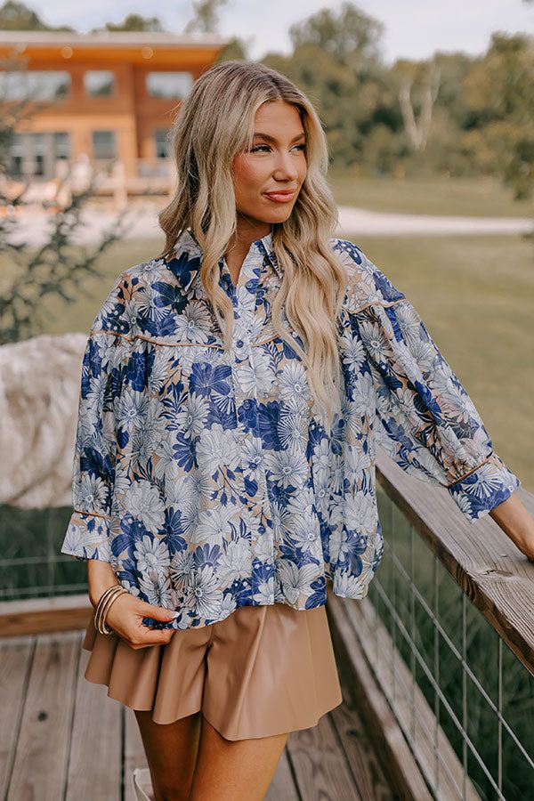 - Channel flower power vibes with this adorable top! Featuring airy floral fabric and a playful collared neckline, this flowy beauty brings a touch of whimsy to your OOTD. Slip it on and feel effortlessly fabulous, no matter where your day takes you! - Sheer organza material with a white, sapphire, and gold colored floral print - A collared neckline - A button up neckline - Gold colored accent trim with a satin finish on the yoke and sleeve cuffs - ¾ length sleeves with button closure cuffs - A Blue Button-up Blouse With Floral Print, Chic Tops With Floral Print And Collared Neckline, Blue Floral Print Top For Garden Party, Blue Floral Print Button-up Top, Blue Collared Blouse For Vacation, Vacation Floral Print Button-up Blouse, Breezy Blue Spring Tops, Blue Tops For Summer Garden Party, Blue Summer Blouse With Collared Neckline