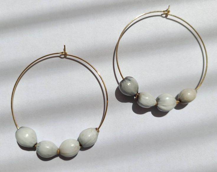 "This minimalist design consists of 14K gold filled hoop earrings with Job's Tears beading. Job's tears are a natural product made from the seeds of a plant that grows in tropical regions. They come in natural shades of white and gray and vary in shape and size because they are in their natural form. Named after Job, the biblical character in the Old Testament, who endured great suffering. There is unanimous agreement that the shape of these beads represents tears, however \"whose\" tears is a p Gift Hoop Earrings With Large Beads, Adjustable Large Beaded Hoop Earrings As Gift, Round Hoop Earrings With Large Beads For Gifts, Round Hoop Earrings With Large Beads, Large Beaded Hoop Earrings As A Gift, Large Beads Hoop Earrings As Gift, Hoop Earrings With Large Beads For Gifts, Hoop Earrings With Large Beads As Gift, Small Hoop Earrings With Large Beads As Gift