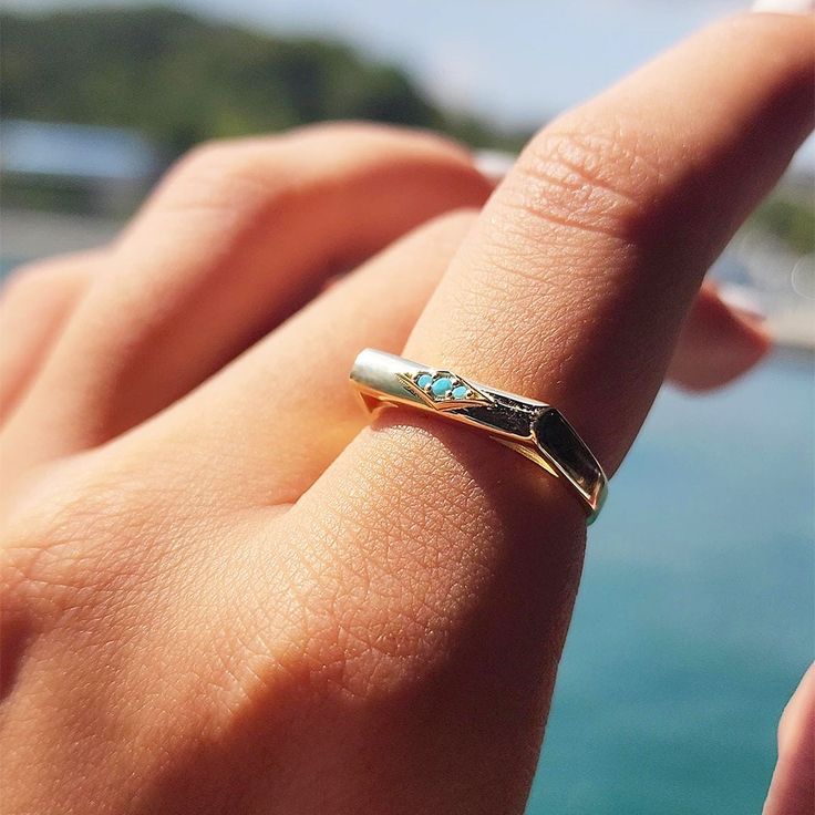 a person's hand with a gold ring on their finger and the ocean in the background