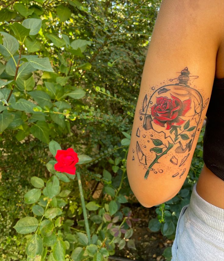 a woman with a rose tattoo on her arm next to a bush and red rose