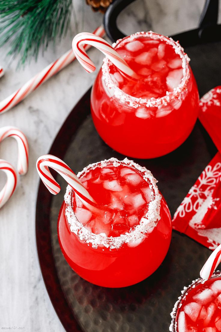 two red drinks with candy canes on the rim and peppermint garnishes