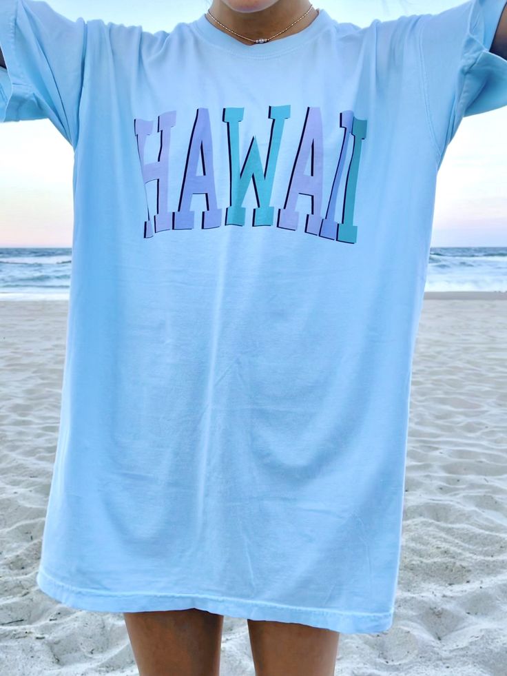 "Such a cute tee for summer! Comfort Colors chambray (light blue) t-shirt with \"HAWAII\" in blue and purple, with a black outline. Model is 5'4\" and wearing a size XL for an oversized look. 100% cotton." Light Blue Short Sleeve T-shirt For Summer, Casual Light Blue T-shirt For Summer, Trendy Blue Pre-shrunk T-shirt, Light Blue Letter Print T-shirt For Spring, Casual Light Blue Screen Print T-shirt, Light Blue Text Print Crew Neck T-shirt, Light Blue Short Sleeve T-shirt With Text Print, Blue Summer T-shirt For Vacation, Light Blue Fun T-shirt With Graphic Print