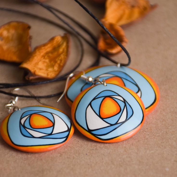 two orange and blue earrings sitting on top of a table next to an orange leaf