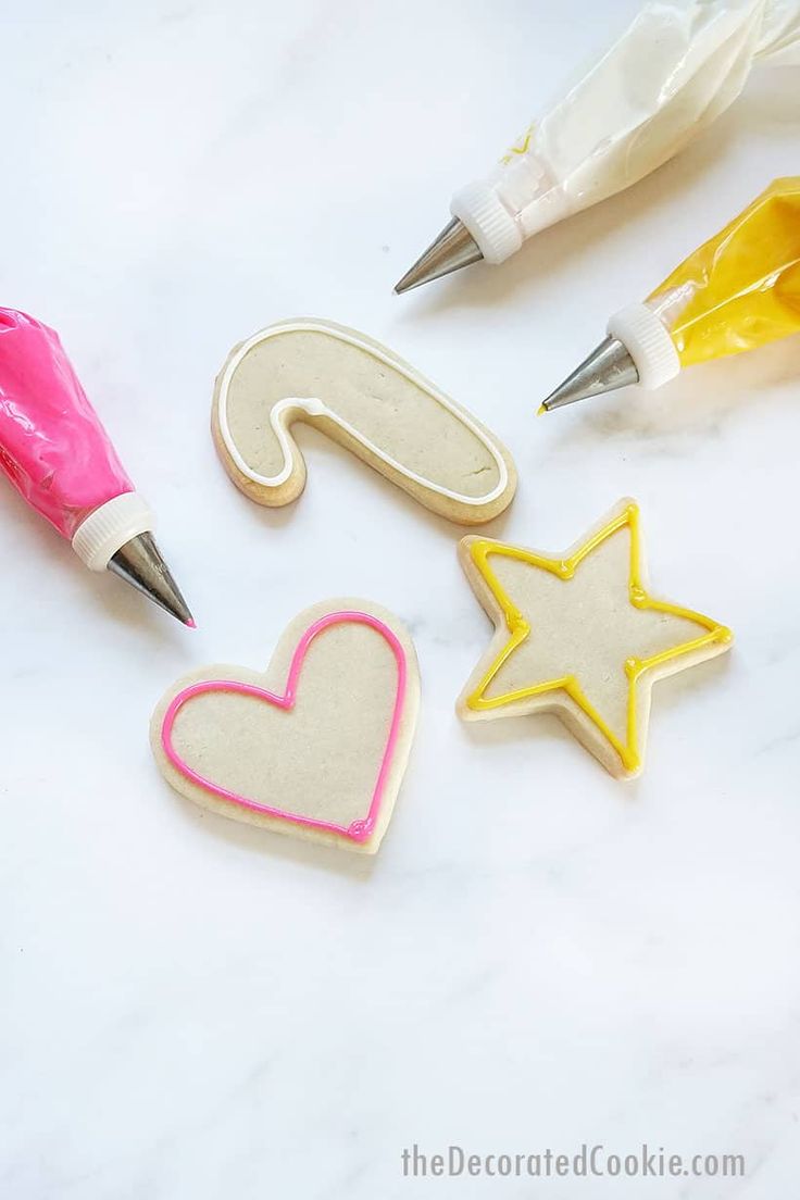 three decorated cookie cutters sitting on top of a white table next to pens and markers