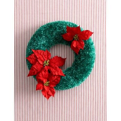 a green wreath decorated with poinsettis on top of a striped table cloth