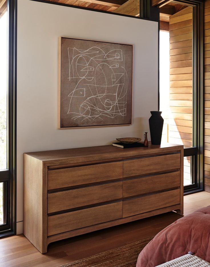 a bedroom with a large painting on the wall and wooden dresser in front of it