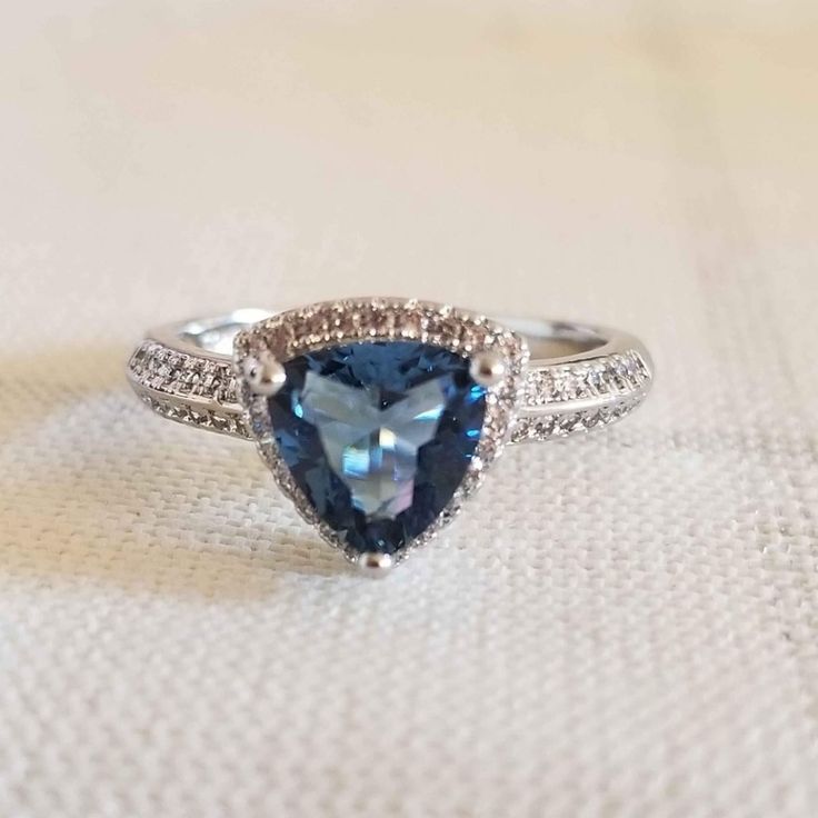 a blue and white diamond ring on top of a cloth covered table with a white background