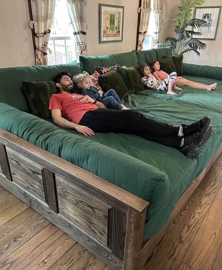 three people lounging on a green couch in a living room with wood flooring