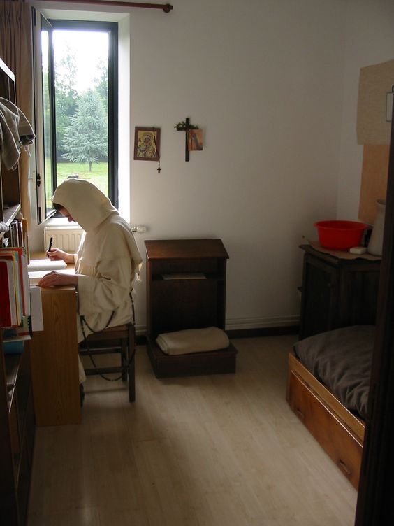 a person in a room with a bed and some shelves on the wall, near a window