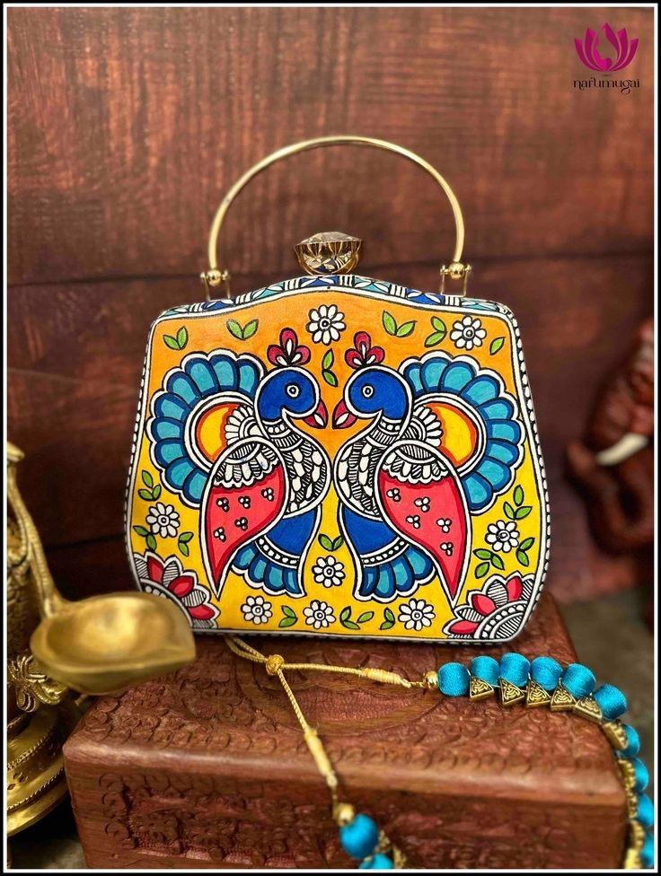 a colorfully painted purse sitting on top of a wooden box next to a gold necklace