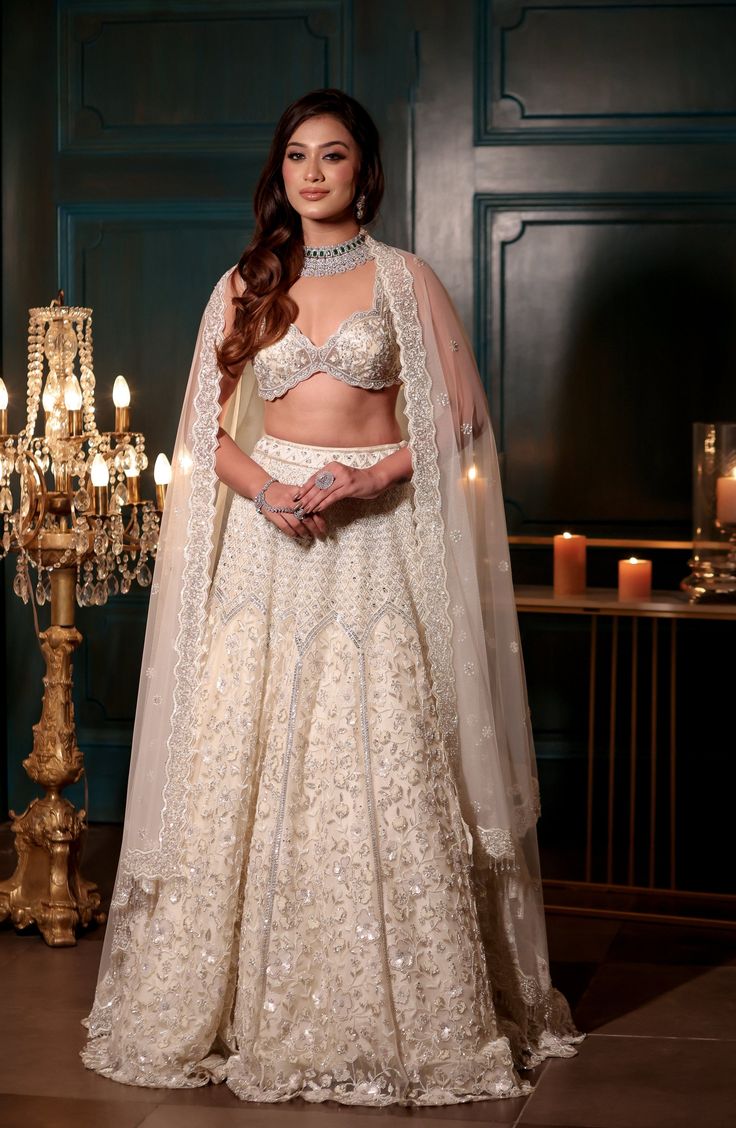 This delicate ivory lehenga features all over sequin, cutdana, crystal and pearl embroidery paired with a strappy embroidered blouse. The embroidered dupatta is crafted in net.DELIVERY TIMEPlease allow 8-12 weeks for your outfit to arrive.FABRIC DETAILSNetProfessional cleaning only. Glamorous Organza Lehenga With Pearl Embroidery, Glamorous Wedding Traditional Wear With Resham Embroidery, Reception Lehenga In Off White With Sheer Dupatta, Off White Lehenga With Sheer Dupatta For Reception, Glamorous Dupatta With Pearl Embroidery For Festive Occasions, Glamorous Semi-stitched Dupatta With Intricate Embroidery, Cream Bollywood Lehenga With Pearl Embroidery, Bollywood Style Cream Lehenga With Pearl Embroidery, Cream Choli With Pearl Embroidery For Reception