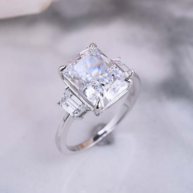 an engagement ring with a princess cut diamond surrounded by baguettes on a marble surface