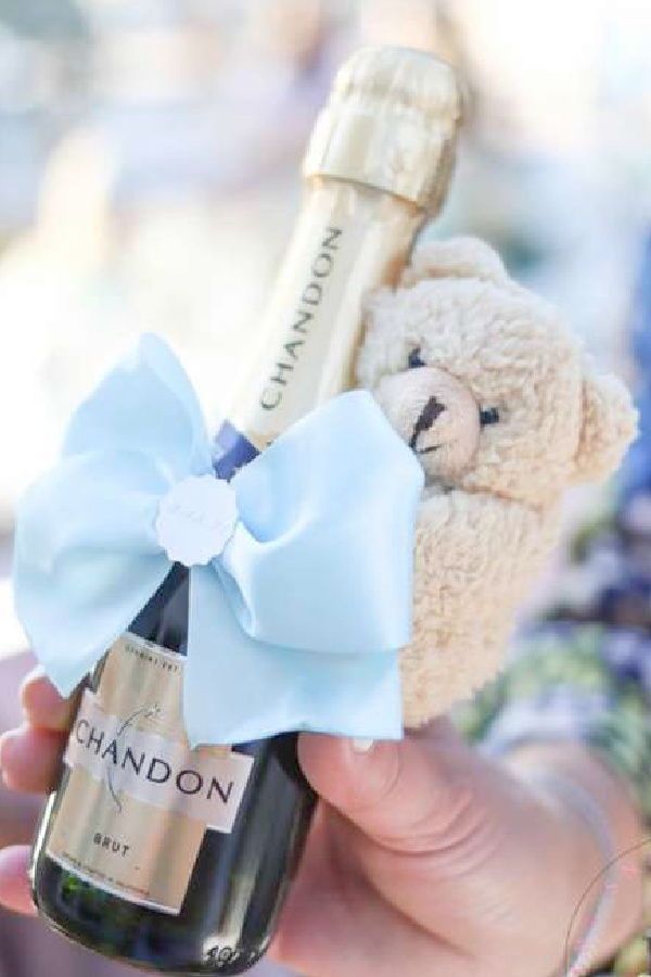 a person holding a bottle of wine and a teddy bear with a bow on it