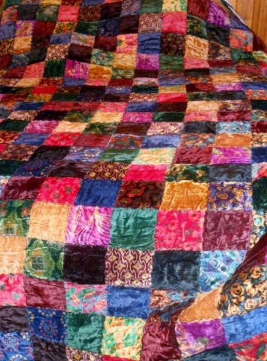 a multicolored quilt on a bed with wooden headboard