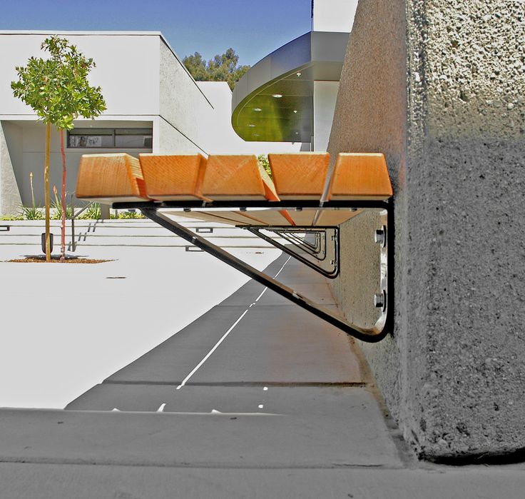 an orange bench sitting on the side of a cement wall next to a tree and building