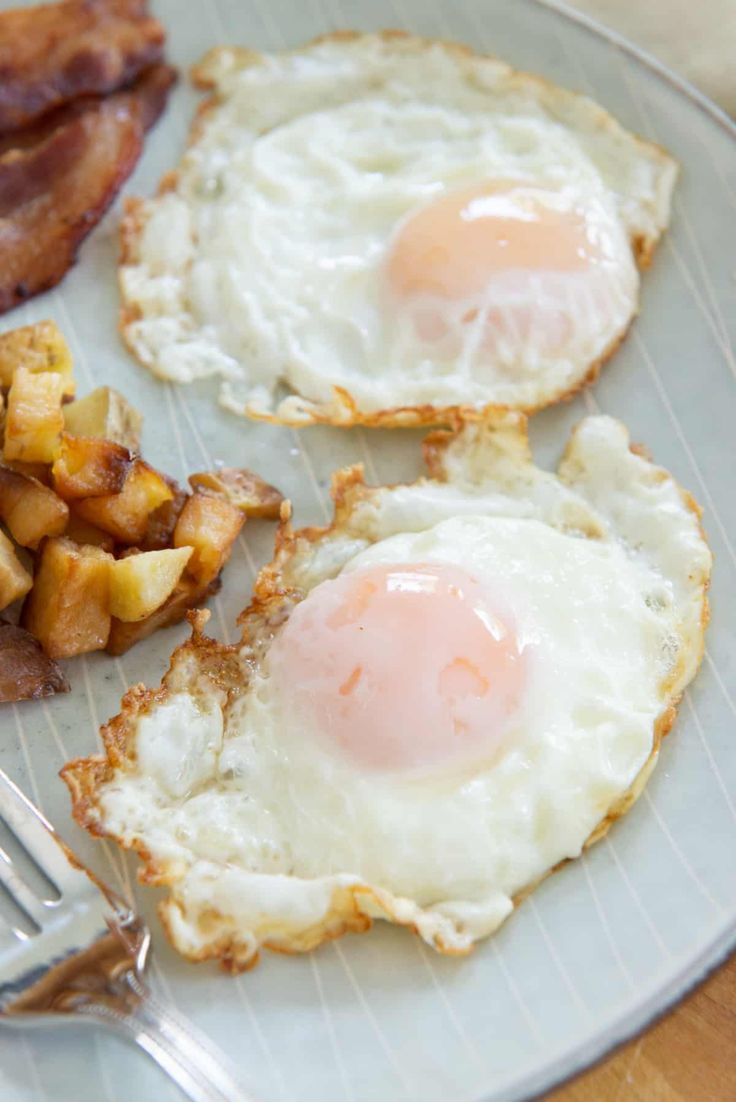 two fried eggs and some potatoes on a plate with a fork next to the plate