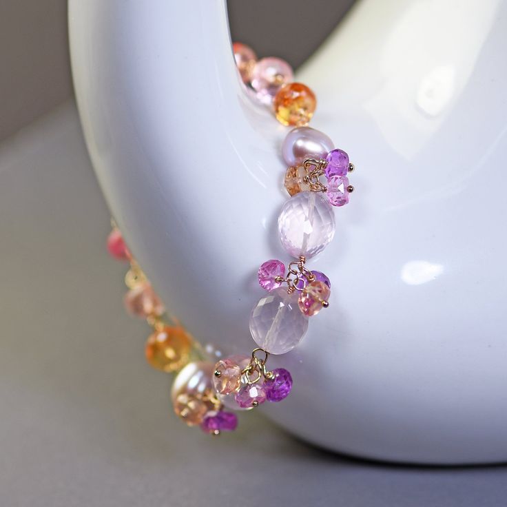 Chunky, statement bracelet in delicate pink, purple and gold hues.  This wire wrapped bracelet is created with beautiful, pastel pink, micro faceted ovals of rose quartz embellished with clusters of pink topaz, purple and gold sapphire clusters between them, lustrous pink pearls and colorful faceted sapphire roundels. These pretty gems are arranged into a colorful row. This bracelet closes with a gold filled spring ring clasp and it has an extender with a lemon quartz charm. Adjustable from 7.25 Elegant Pink Bracelets With Natural Stones, Pink Jubilee Bracelet With Round Beads, Pink Round Crystal Gemstone Bracelet, Pink Crystal Gemstone Bracelet, Pink Gemstone Crystal Bracelet, Pink Natural Stones Crystal Bracelet, Delicate Pink Round Bracelets, Pink Jubilee Beaded Bracelet, Pink Gemstone Beaded Bracelets For Jewelry Making