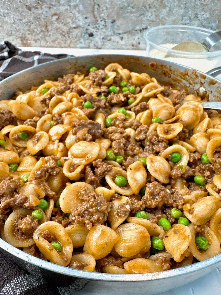 a skillet filled with pasta and peas on top of a table next to utensils