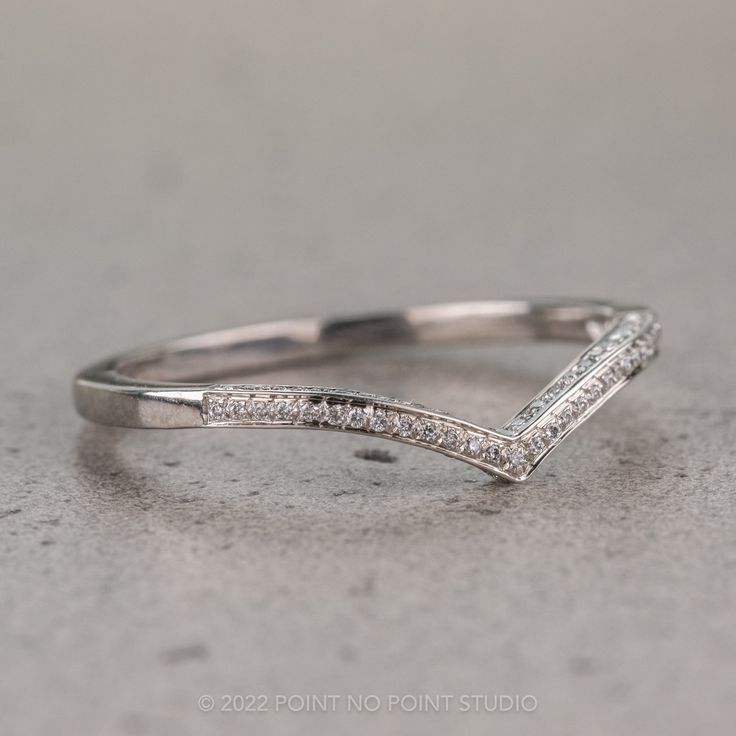 a white gold wedding band with pave set diamonds on the side, in front of a gray background