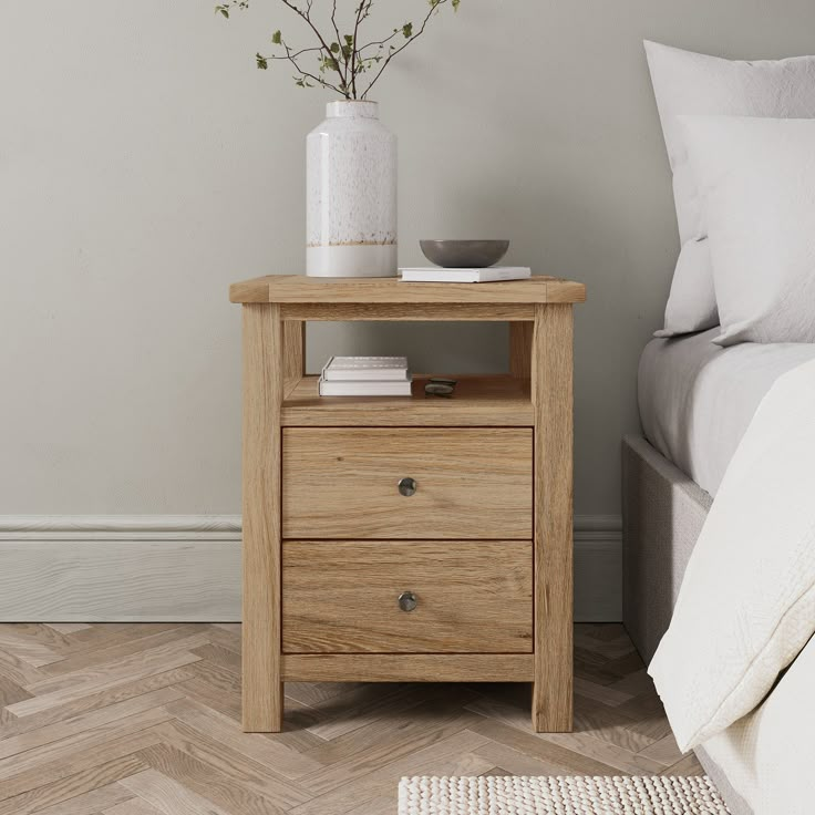 a wooden night stand with two drawers and a white vase on the nightstand next to it