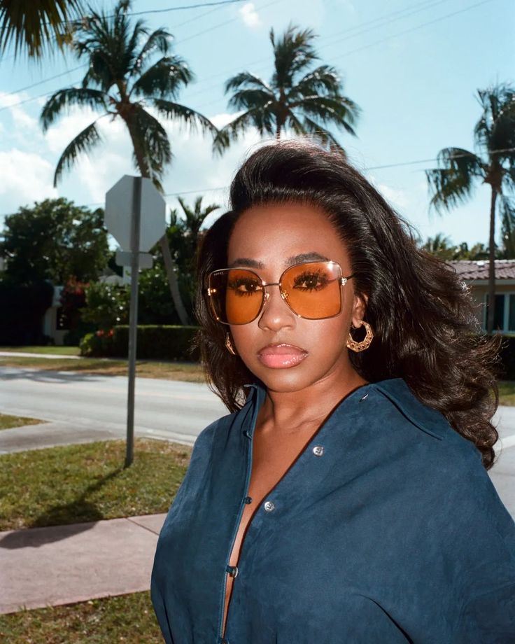 a woman wearing sunglasses standing in front of palm trees