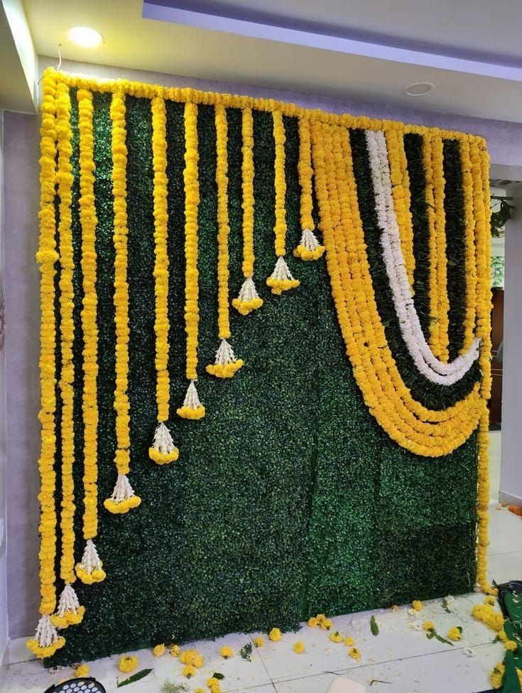 yellow and white garlands hanging from the side of a green wall with flowers on it