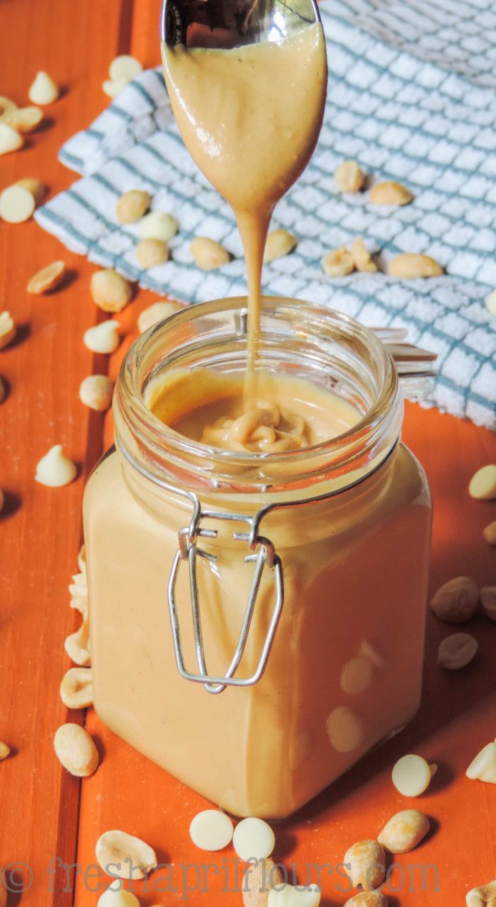 peanut butter being poured into a jar with peanuts scattered around it on a wooden table