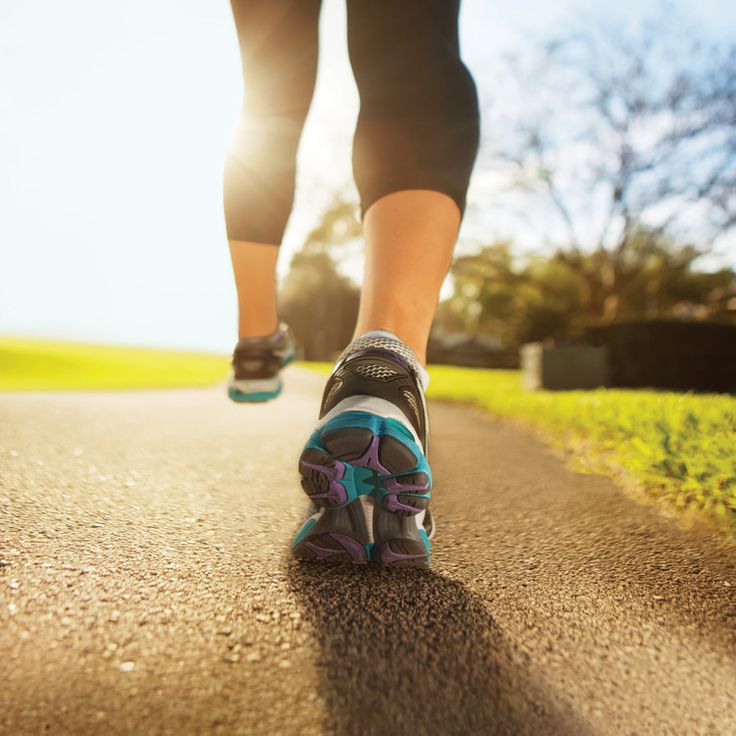 a close up of a person's feet running on a road with grass and trees in the background