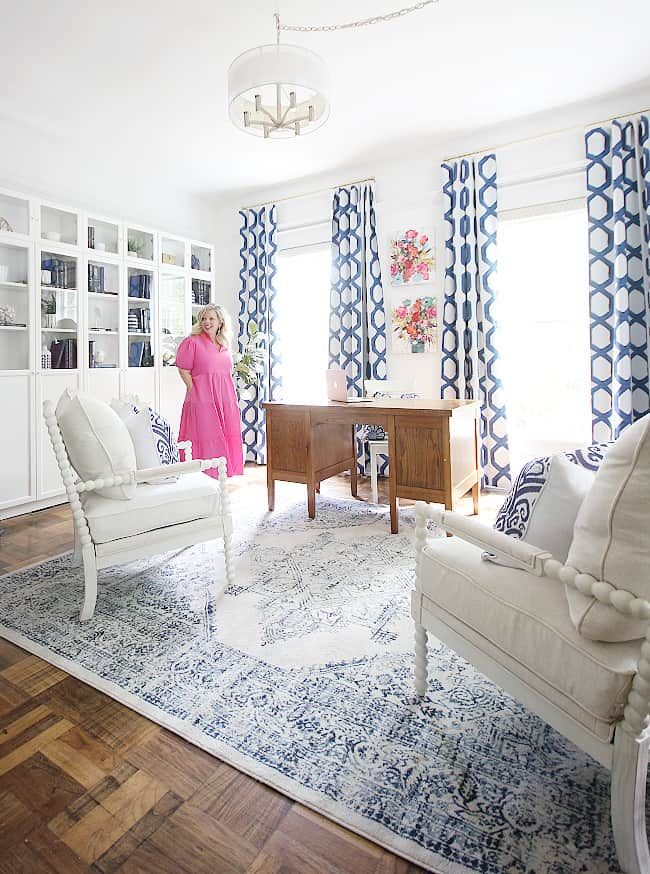 a woman standing in a living room with blue and white curtains