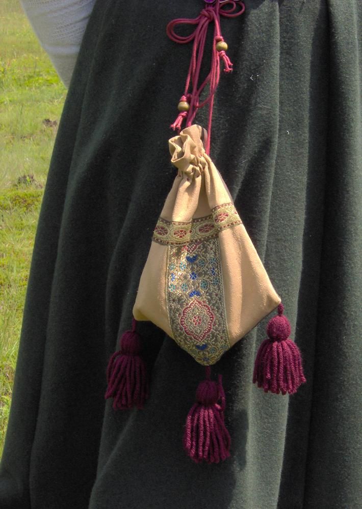 a woman wearing a long skirt and holding a bag with tassels on it